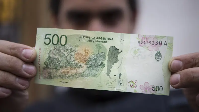 Pessoa segura uma nota de peso-argentino
