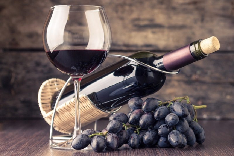 Taça de vinho ao lado de um cacho de uvas e uma garrafa de vinho ao fundo