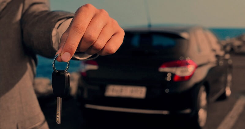 Pessoa segura as chaves de um carro em frente ao veículo