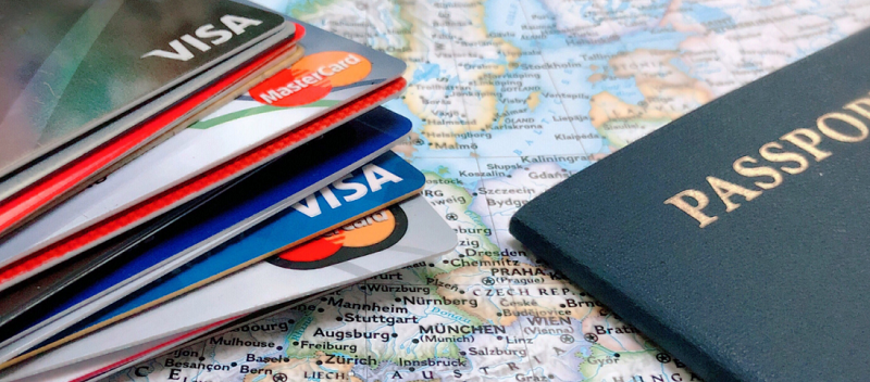 Cartões de crédito empilhados ao lado de um passaporte, ambos estão em cima de um mapa