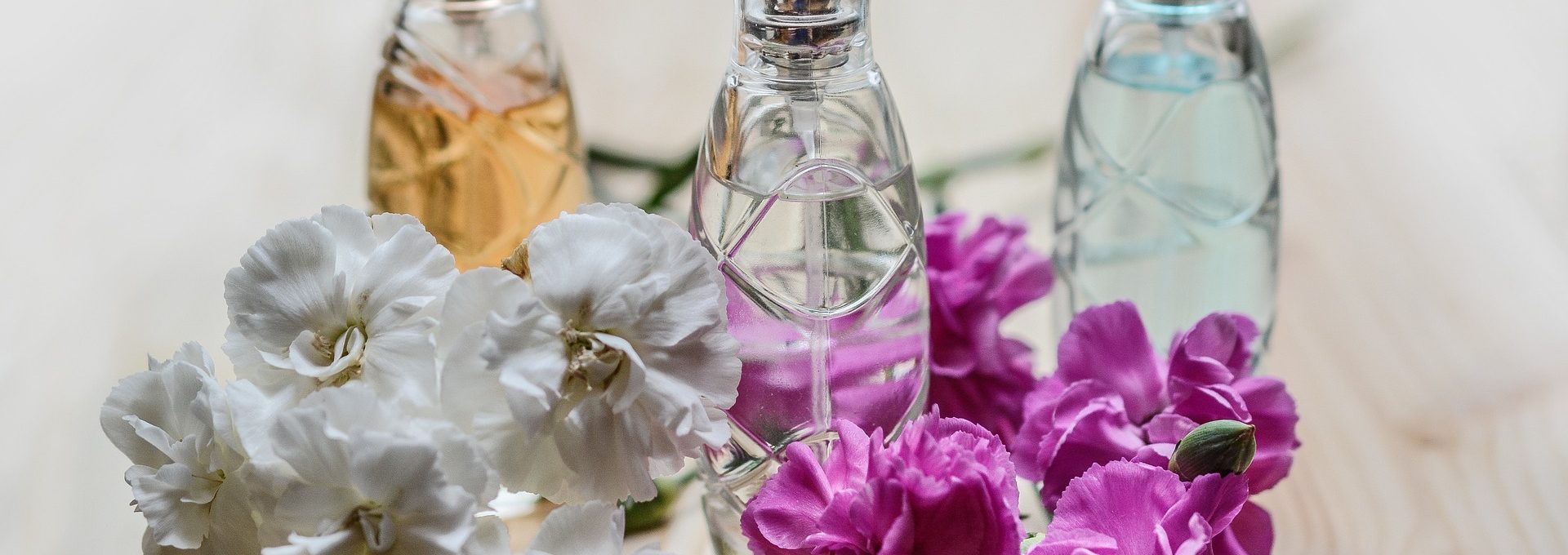 Três vidros de perfume com cachos de flores ao redor