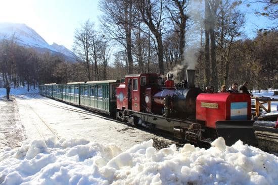 Trem do Fim do Mundo em Ushuaia andando em meio a neve. É possível notar árvores ao redor.