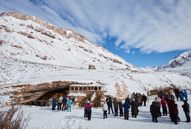 Turistas em montanha com neve em Mendoza. Nota-se uma casa no meio do lugar
