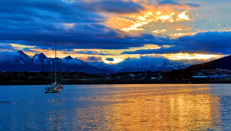 Pôr do sol em Ushuaia, nota-se montanhas ao fundo e um lago em primeiro plano com um barco.