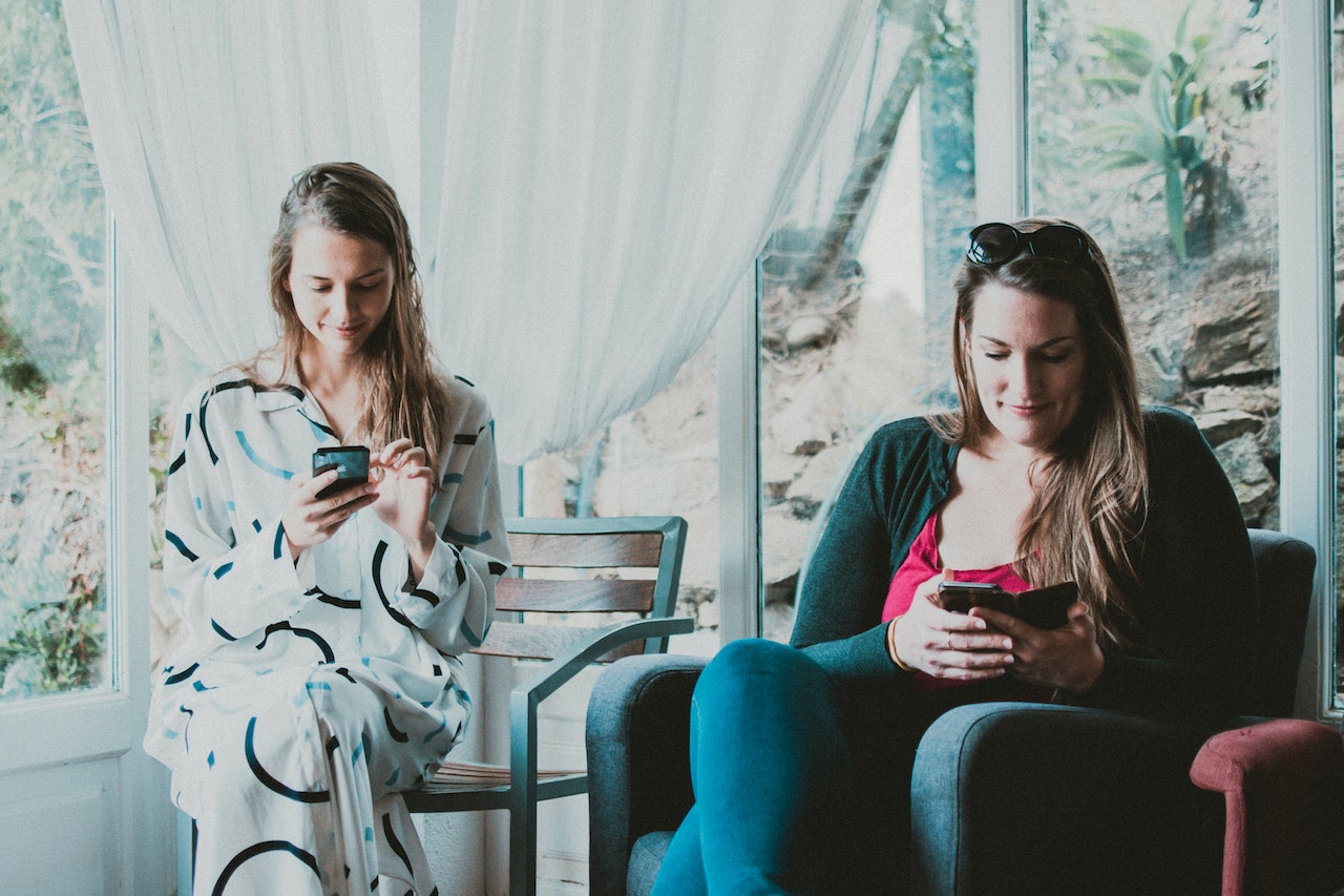 Duas mulheres estão sentadas e mexendo no celular