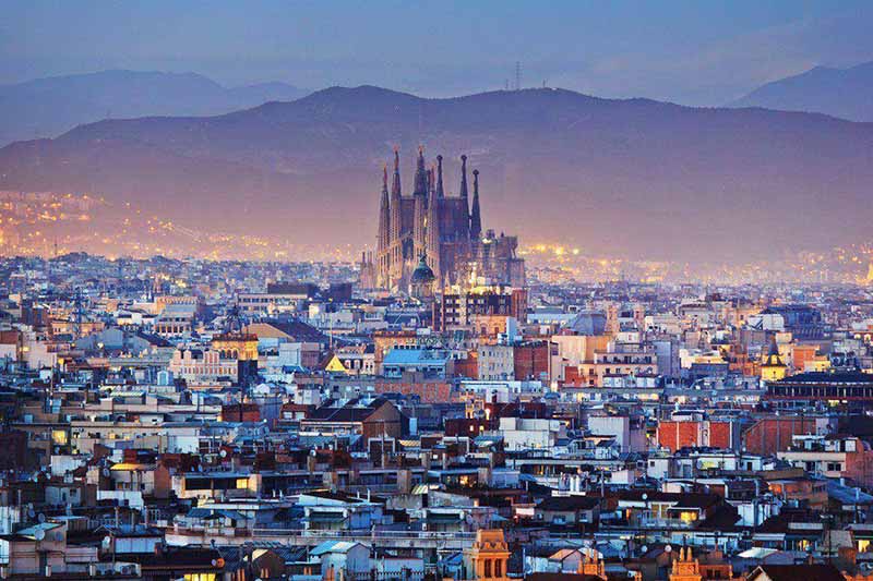 Vista da ciade de Barcelona no inverno, ao fundo estão montanhas e em meio à noite, nota-se a cidade iluminada