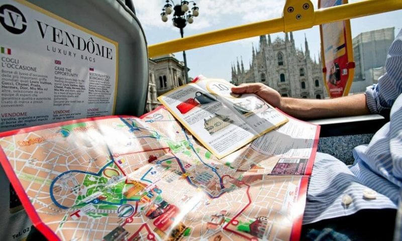 Pessoa segura mapa dentro de ônibus turístico em Milão.