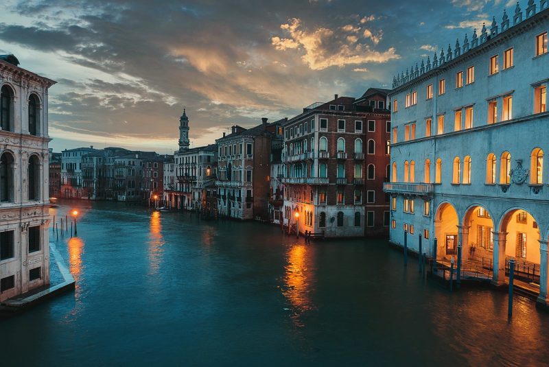 Vista da cidade de Veneza à noite. Os prédios estão com pouca iluminação, pois começa a anoitecer.