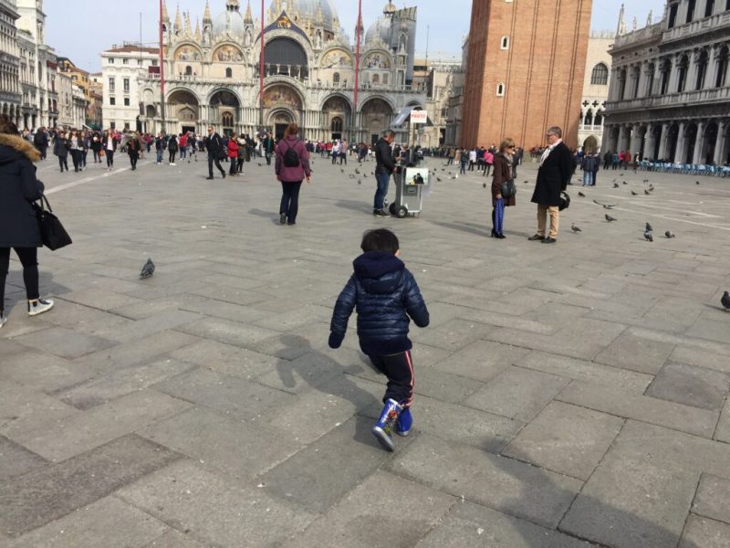Menino pequeno corre na Praça São Marcos em Veneza.