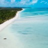 An aerial shot of a clear blue sea with a forested shore and beach on the side